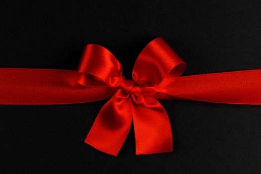 Red satin ribbon bow on black paper background