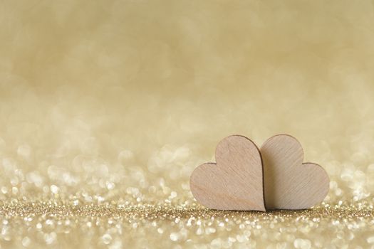 Two small handmade wooden hearts on bright golden lights bokeh background Valentines day card