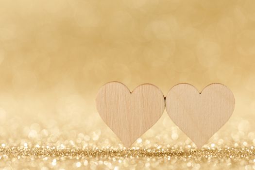 Two small handmade wooden hearts on bright golden lights bokeh background Valentines day card