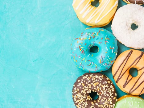 Top view of assorted donuts on blue concrete background with copy space. Colorful donuts background. Various glazed doughnuts with sprinkles.