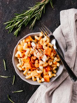 Fusilli pasta with pumpkin, rosemary and brie cheese. Idea recipe pasta. Vegetarian food. Homemade pasta dish in gray bowl over black concrete background. Copy space. Top view or flat lay.