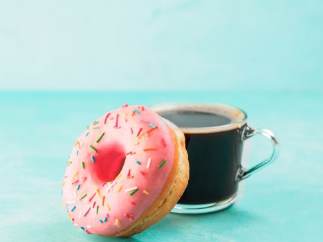 Pink donut and coffee on blue concrete background with copy space. Glazed doughnut and coffee cup with copyspace