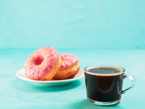 Two pink donuts and coffee on blue concrete background with copy space. Colorful donuts in plate and coffee cup with copyspace. Glazed doughnuts with sprinkles