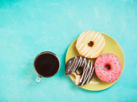 Top view of assorted donuts and coffee on blue concrete background with copy space. Colorful donuts on plate and coffee background. Various glazed doughnuts with sprinkles.