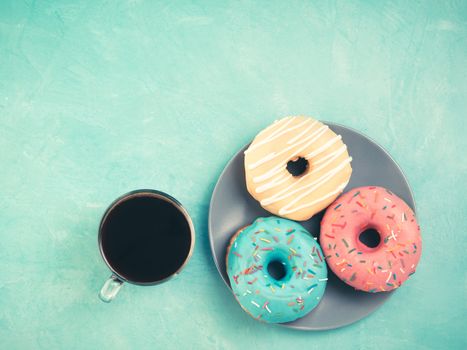 Top view of assorted donuts and coffee on blue concrete background with copy space. Colorful donuts on plate and coffee background. Various glazed doughnuts with sprinkles. Toned image