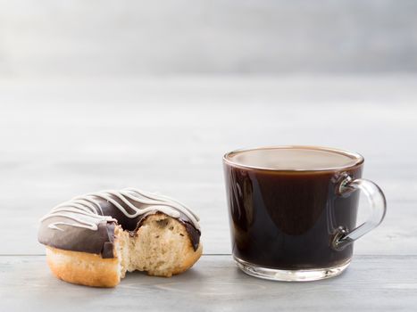 Close up view of chocolate donut and coffee on gray wooden background with copy space. Glazed doughnuts and coffee on grey wooden table with copyspace.