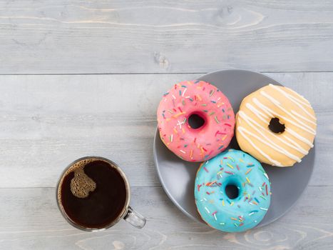 Top view of assorted donuts and coffee on gray wooden background with copy space. Colorful donuts and coffee background with copyspace. Various glazed doughnuts with sprinkles on grey wooden table.