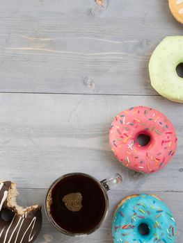 Top view of assorted donuts and coffee on gray wooden background with copy space. Colorful donuts and coffee background with copyspace. Various glazed doughnuts with sprinkles on grey wooden table.