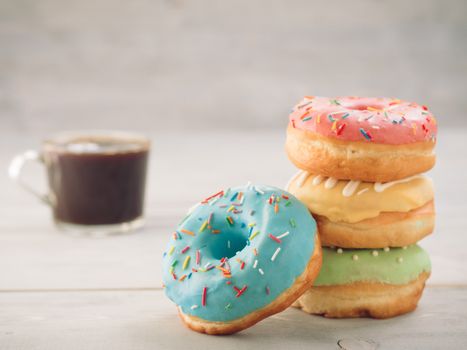 Donuts and coffee on gray wooden table with copy space. Colorful donuts and coffee cup on grey wooden background with copyspace. Glazed doughnuts in stack on foreground and coffee on background