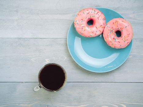 Top view of assorted donuts and coffee on gray wooden background with copy space. Two pink donuts on blue plate and coffee background with copyspace. Smile sign, good morning concept