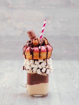 Chocolate and donuts extreme milkshake with marshmallow and other sweets in mason jar on gray wooden background. Crazy freakshake on gray wooden table with copy space