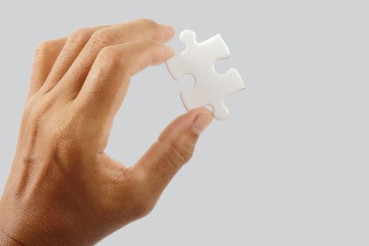 Male hand holding white puzzle isolated on gray background, clipping path.