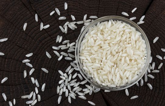 Bowl of rice groats on black wooden background, top view