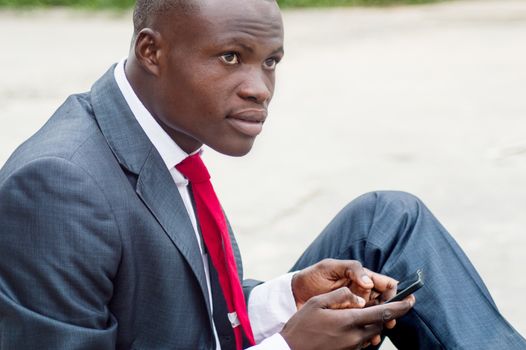 Portrait of young man sitting outside and manipulating his mobile phone