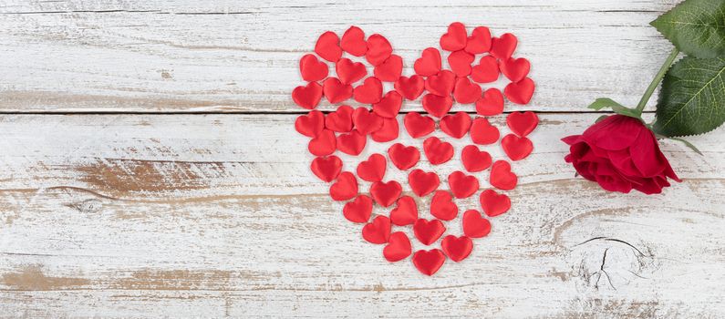 Filled red heart shapes and single rose on rustic white wood in flat lay view