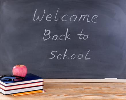 Back to school concept with welcome back to school message on erased black chalkboard plus desktop and supplies.  