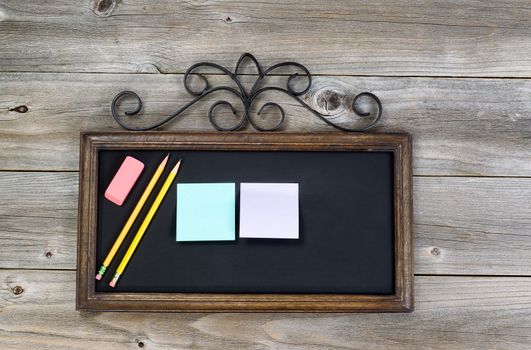 Old fashion chalkboard, pencils, eraser and paper notes on rustic wood. Layout in horizontal format.
