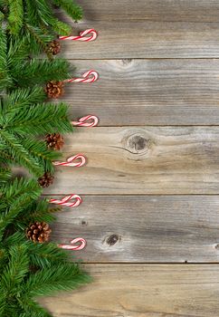 Christmas border with pine tree branches, and candy canes on rustic wooden boards. Layout in vertical format.  