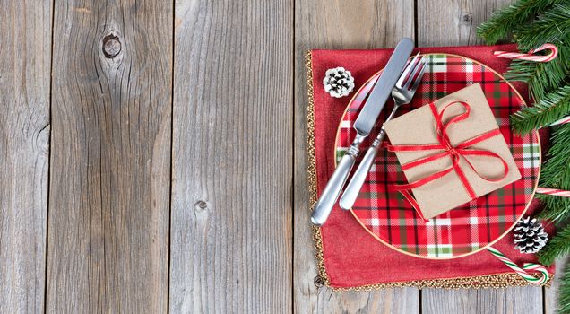 Festive Christmas dinner setting with evergreen branches and gift on top of rustic wood. Top view with copy space. 