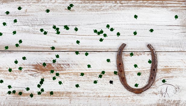 St Patrick day good luck horseshoe with shiny clovers on rustic white wooden boards in overhead view 