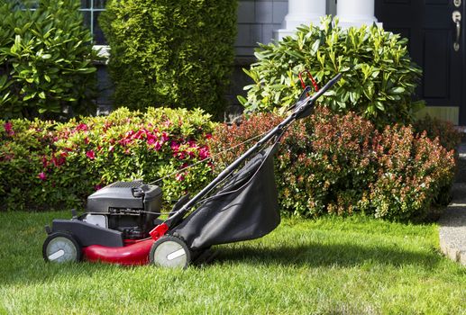 Horizontal photo of old gas lawnmower on front yard with home in background