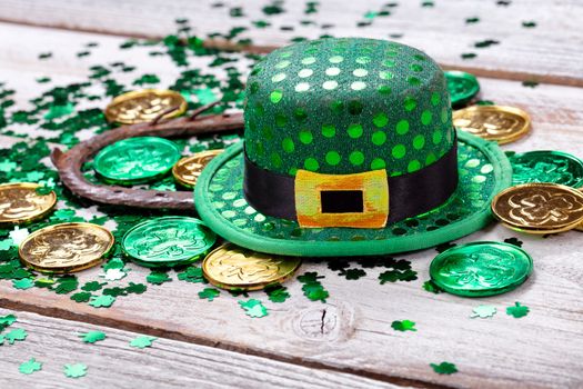 Bright green hat with gold coins, shamrock and rusty horseshoe for Saint Patrick Day on white rustic wooden background in close up format  