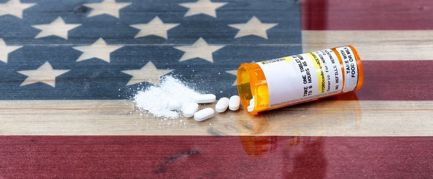 Bottle of prescription for Hydrocodone or generic opioid with crushed or whole pain killer tablets. Rustic USA flag in background for drug addiction concept in America  