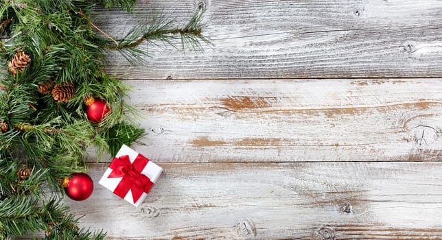 Rough fir branches with Christmas ball ornaments and giftbox on rustic white wooden boards 