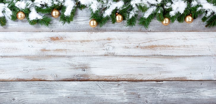 Top border of snow covered Christmas evergreen branches and Golden ornaments on white vintage wood