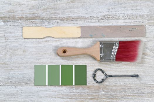 Paint brush with used stick, lid opener, and paint color choice on old white wooden boards