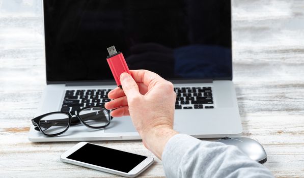 Close up of male hand holding USB Thumb drive with workstation technology in background for business or education use 