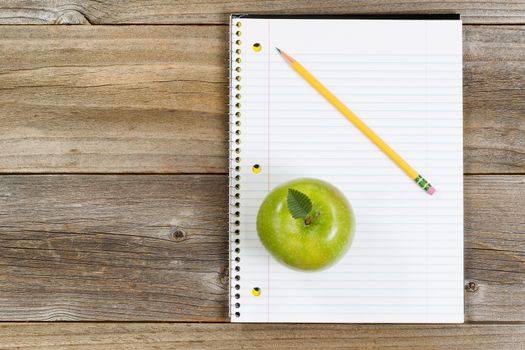 Top view of green apple, notepad and pencil on rustic wood.