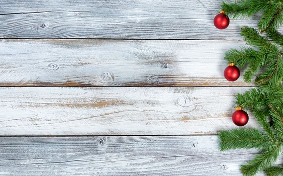 Traditional Christmas evergreen branches with red ornament decorations on rustic knotty wood in flat lay format