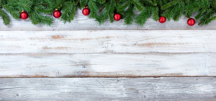 Top border of Christmas evergreen branches and red ornaments on white vintage wood