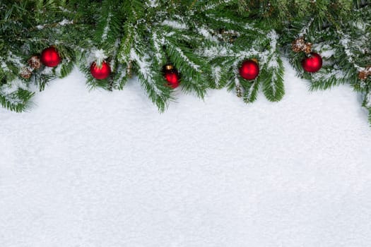 Evergreen branches and red ornaments covered in snow. Christmas concept with plenty of copy space. 