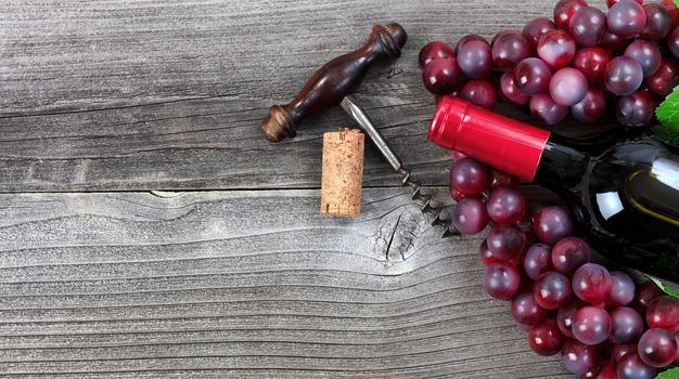 Unopen bottle of red wine and grapes on vintage wood