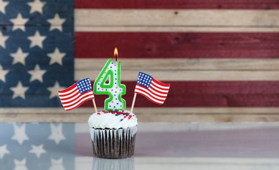 Chocolate cupcake and number four candle and small USA flags with rustic wooden United States Flag in background. July 4th holiday concept. 