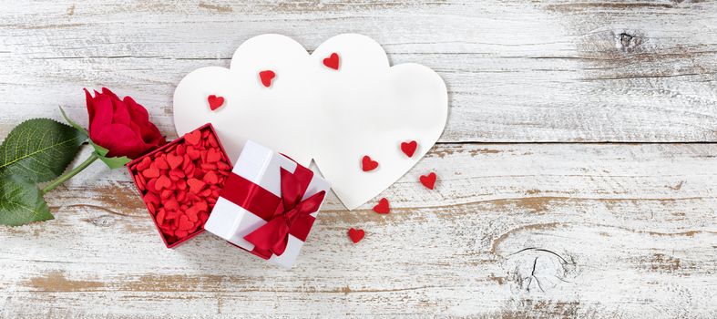 Valentines card, rose and gift box filled with candy small heart shapes on rustic white wood in flat lay view