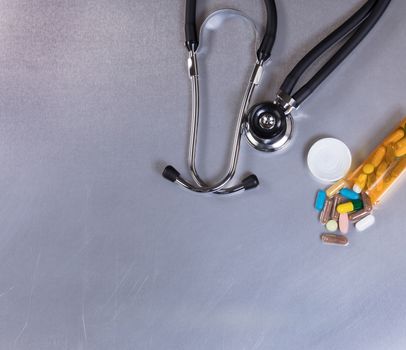 Overhead view of a medical stethoscope and pills on stainless steel table