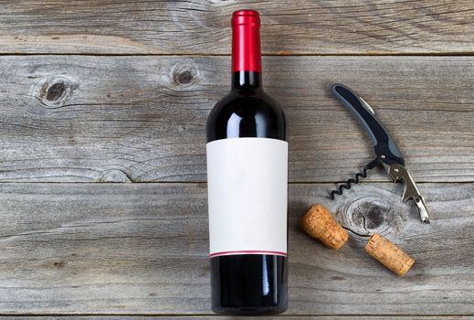 Top view angled shot of red wine bottle with corks and opener on rustic wooden boards