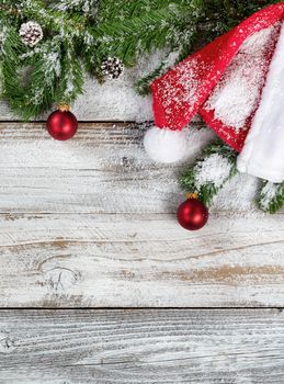 Snowy Christmas fir branches with traditional Santa hat and ornaments on rustic wood in flat lay format