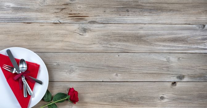 Holiday Dinner setting with single red rose and silverware in lower left corner on rustic wood in flat lay view