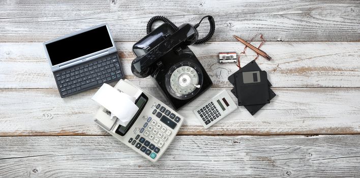 Overhead view of obsolete technologies that includes rotary dial phone and old computer data storage devices plus calculators