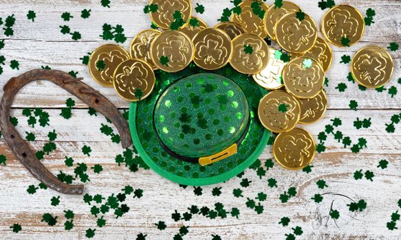 St Patrick good luck hat, green clovers and horseshoe with shiny gold coins on rustic white wooden boards 