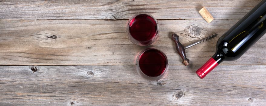 Flat view of a bottle of red wine, antique corkscrew, and full drinking glasses on rustic wooden boards