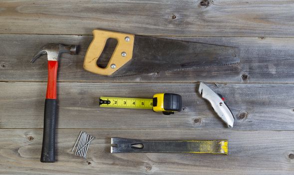 Top view of basic home repair tools consisting of wood saw, hammer, nails, box cutter, pry bar and tape measure on rustic wooden boards