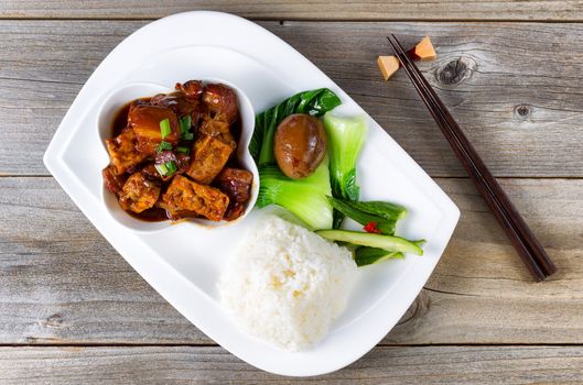 Top view of succulent Chinese dish with fried tofu, bok choy, soy sauce egg, cucumber, rice and chopsticks in holder on rustic wood. 