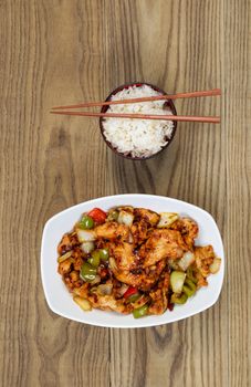 Vertical overhead view of Chinese spicy chicken dish and rice in bowl with chopsticks placed on rustic wooden boards.  