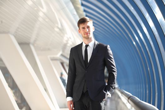 Portrait of happy young businessman standing on office corridor looking at camera