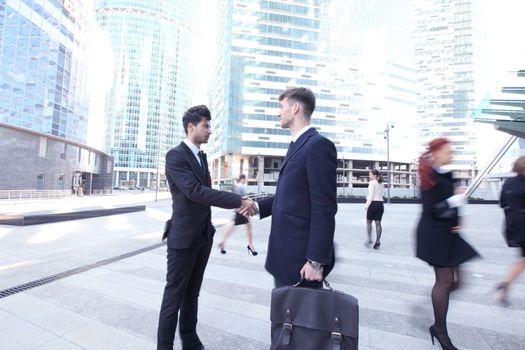 Business people shaking hands in street , crowd around, skyscrapers on background